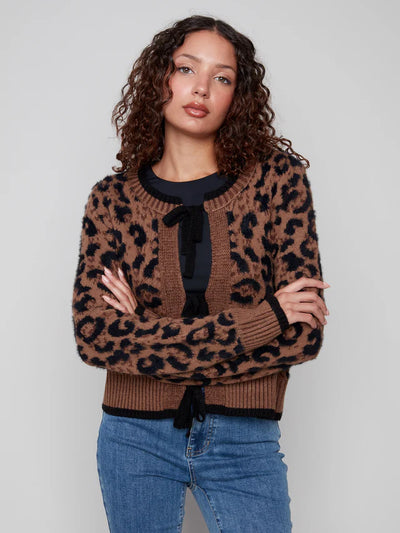 Woman wearing a leopard print sweater with a black tie and blue jeans on a plain background