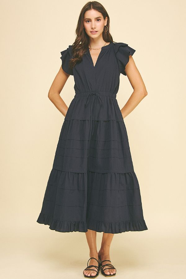 Woman wearing a navy blue dress with ruffled sleeves on a beige background